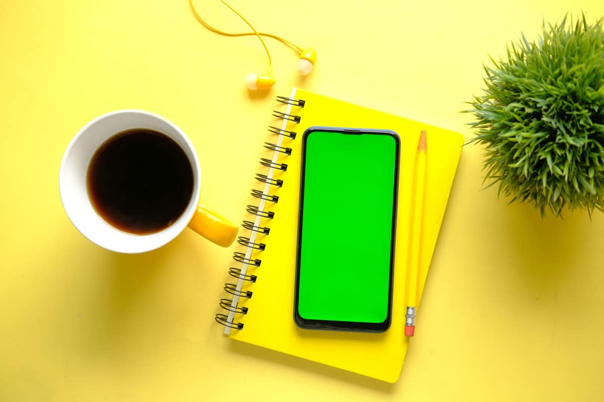 Bright yellow minimalist desk setup with notebook, smartphone, coffee, and plant.
