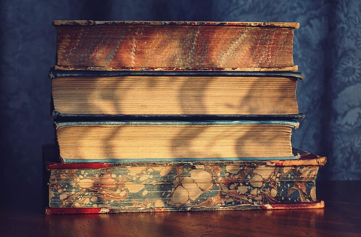 A stack of old vintage books on a wooden table with decorative marbled covers.